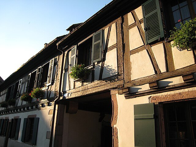 Photo d'une maison traditionnelle à colombages en Alsace (village près du Haut-Kœnigsbourg), illustrant le décor de l'immersion culturelle et des mots alsaciens du terroir.