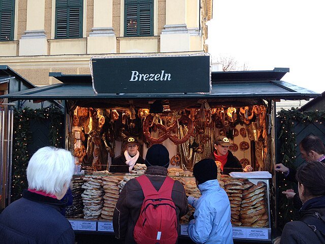 Photo d'un stand de marché de Noël avec une enseigne "Brezeln" et des piles de bretzels, illustrant les mots alsaciens gourmands de la tradition locale.