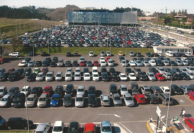 Vue en hauteur d'un grand parking extérieur goudronné et entièrement rempli de voitures en stationnement.